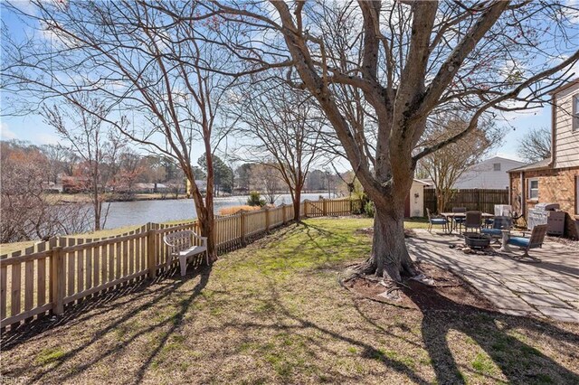 view of yard with a water view, a patio, a fenced backyard, a fire pit, and an outdoor structure