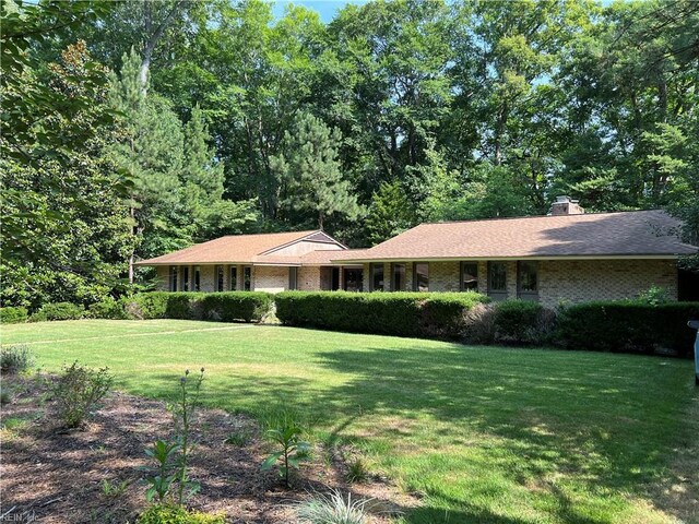 ranch-style home with a chimney, a front yard, and brick siding