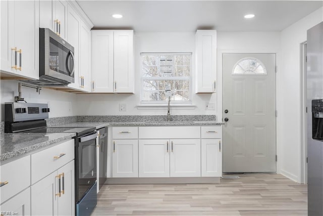 kitchen featuring light stone counters, range with electric cooktop, a sink, stainless steel microwave, and white cabinets