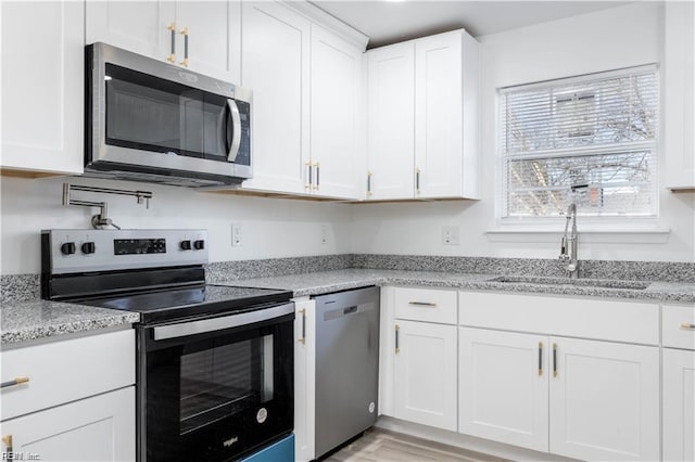kitchen with white cabinetry, a sink, stainless steel appliances, and light stone countertops