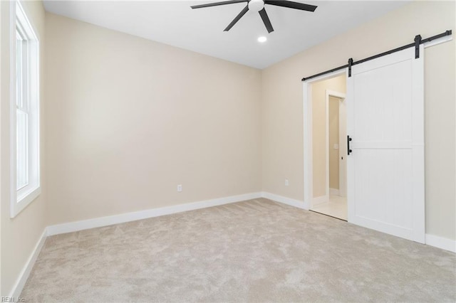 carpeted empty room featuring a barn door, ceiling fan, and a healthy amount of sunlight
