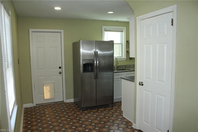 kitchen with baseboards, recessed lighting, dark stone countertops, a sink, and stainless steel fridge with ice dispenser