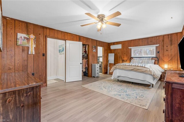 bedroom with light wood-style flooring, wood walls, a wall mounted air conditioner, and ceiling fan