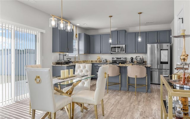 kitchen with a kitchen breakfast bar, decorative light fixtures, light wood-type flooring, light stone countertops, and appliances with stainless steel finishes