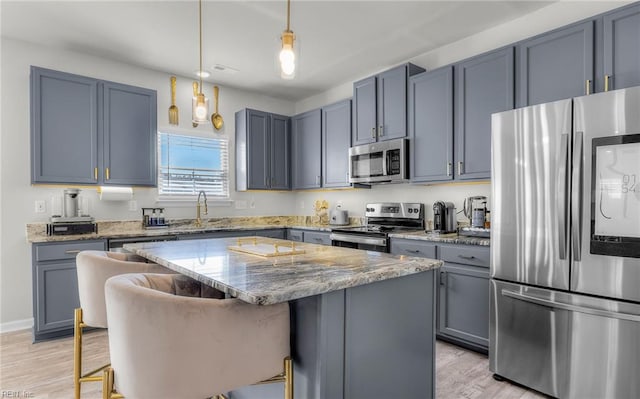 kitchen with light wood-style flooring, light stone countertops, a kitchen island, appliances with stainless steel finishes, and a kitchen breakfast bar