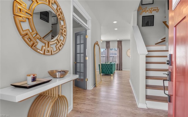 hallway featuring baseboards, stairs, recessed lighting, and light wood finished floors