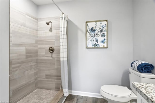 full bathroom featuring toilet, baseboards, a tile shower, and wood finished floors