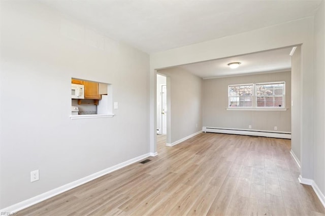 spare room featuring baseboards, visible vents, light wood-type flooring, and a baseboard radiator
