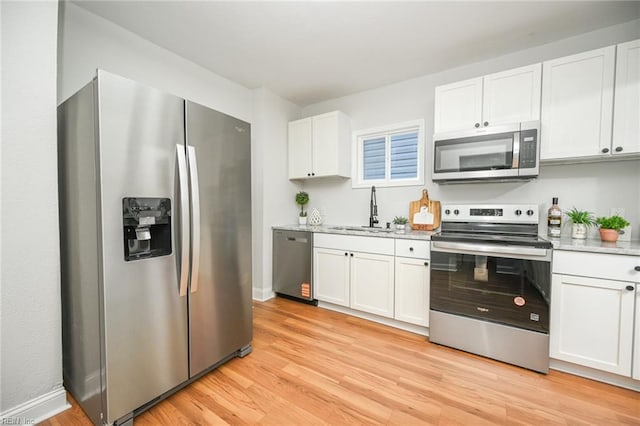 kitchen with light wood-style flooring, baseboards, appliances with stainless steel finishes, white cabinetry, and a sink