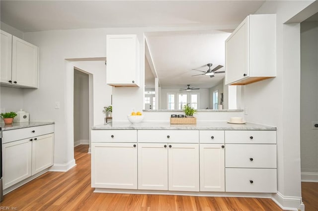 kitchen with light stone countertops, white cabinets, light wood-style flooring, and a ceiling fan