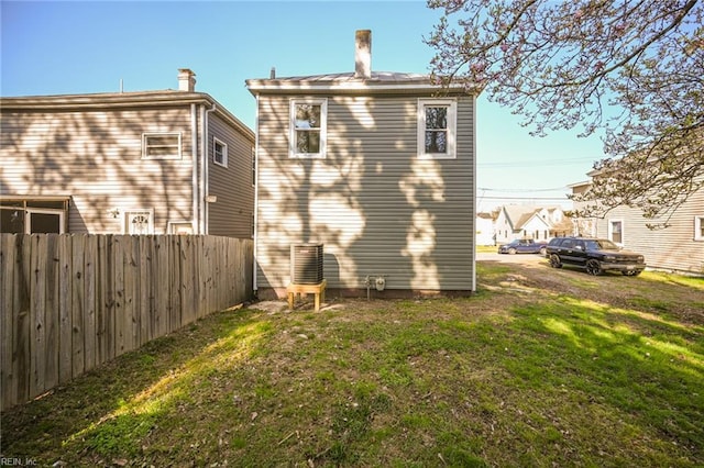 back of house featuring a yard, fence, and a chimney