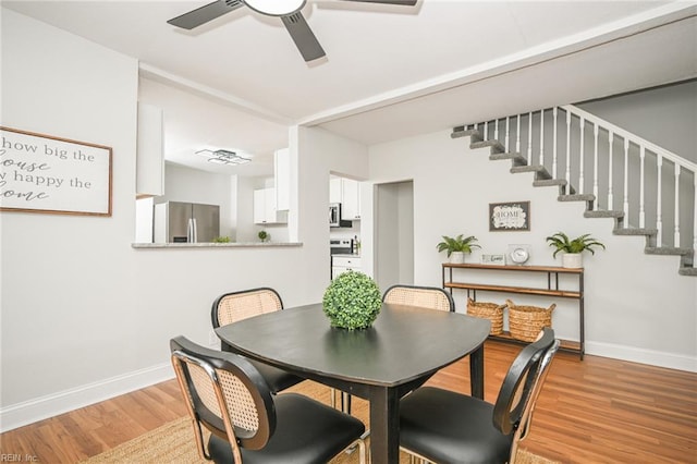 dining area with light wood finished floors, stairs, ceiling fan, and baseboards
