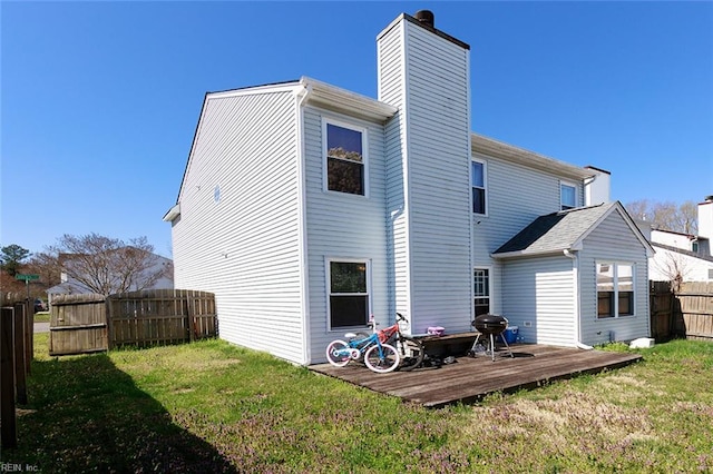 rear view of house featuring a yard, a deck, fence, and a chimney