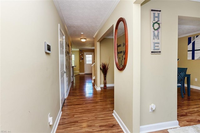 corridor featuring baseboards, a textured ceiling, wood finished floors, and crown molding