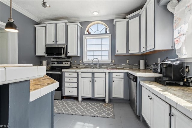 kitchen featuring decorative light fixtures, ornamental molding, stainless steel appliances, a sink, and tile countertops