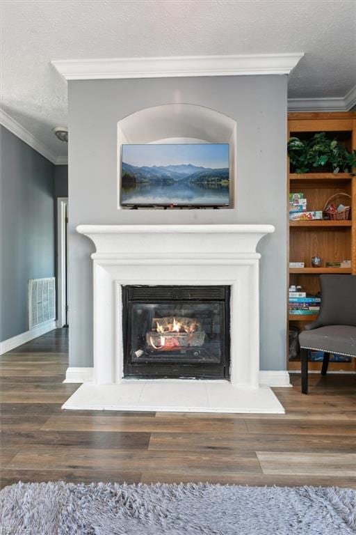 room details featuring visible vents, a glass covered fireplace, crown molding, and wood finished floors