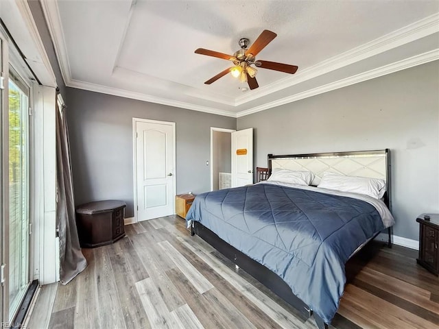 bedroom with baseboards, ornamental molding, wood finished floors, ceiling fan, and a tray ceiling