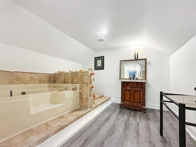 full bath with vanity, a bath, lofted ceiling, visible vents, and wood finished floors