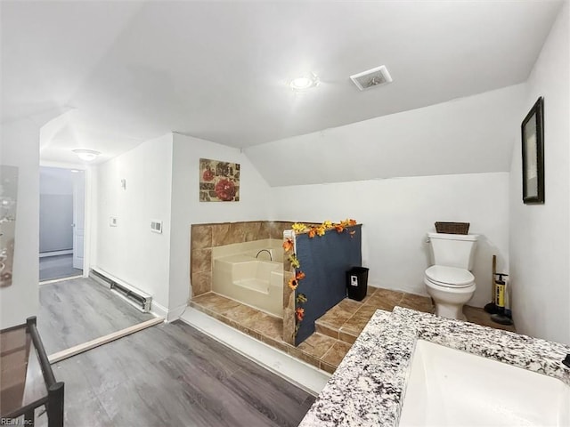 bathroom featuring visible vents, wood finished floors, lofted ceiling, a sink, and a garden tub
