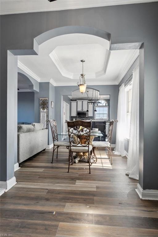 dining room featuring a tray ceiling, ornamental molding, baseboards, arched walkways, and wood finished floors