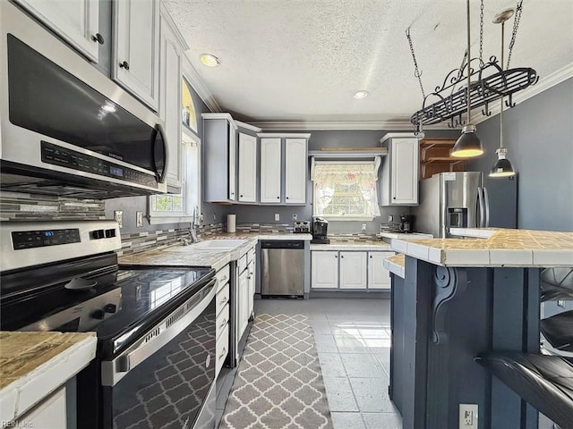 kitchen with crown molding, tile counters, a breakfast bar area, a textured ceiling, and stainless steel appliances