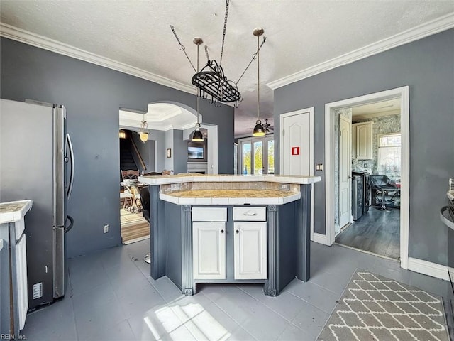 kitchen featuring white cabinetry, crown molding, arched walkways, tile countertops, and freestanding refrigerator