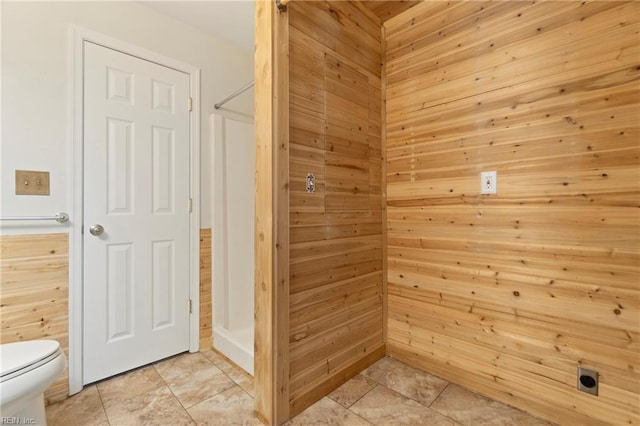bathroom with toilet, wood walls, tile patterned floors, and a shower stall