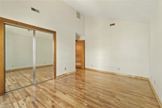 unfurnished bedroom featuring high vaulted ceiling, visible vents, and wood finished floors