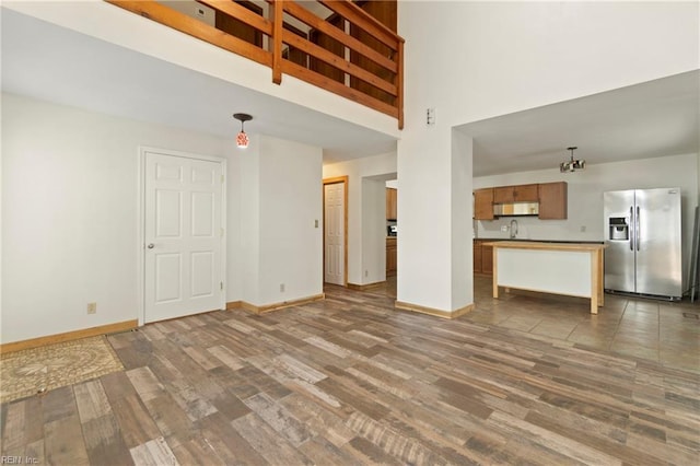 unfurnished living room featuring baseboards, a towering ceiling, and wood finished floors