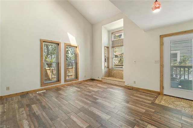 unfurnished room with baseboards, visible vents, high vaulted ceiling, and wood finished floors