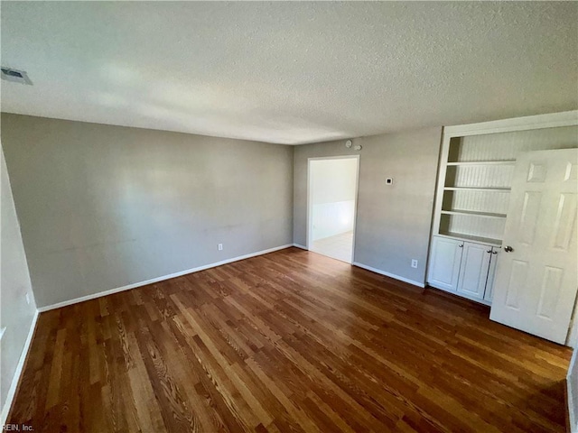 unfurnished bedroom featuring baseboards, a textured ceiling, visible vents, and wood finished floors