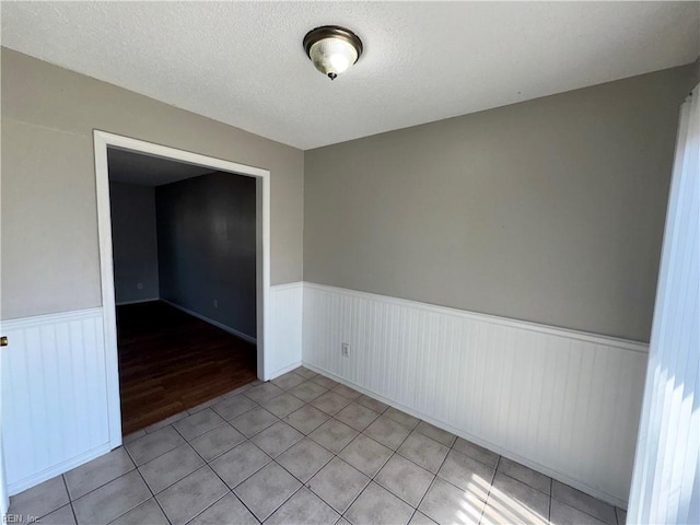 spare room with a wainscoted wall, light tile patterned floors, and a textured ceiling