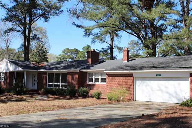 single story home featuring brick siding, concrete driveway, a garage, and a chimney