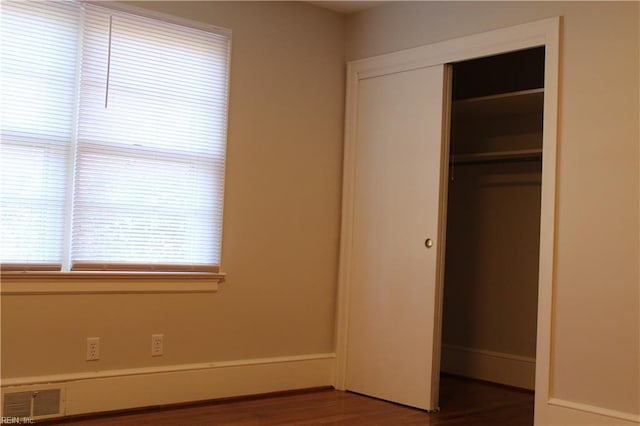 unfurnished bedroom with dark wood finished floors, a closet, and visible vents