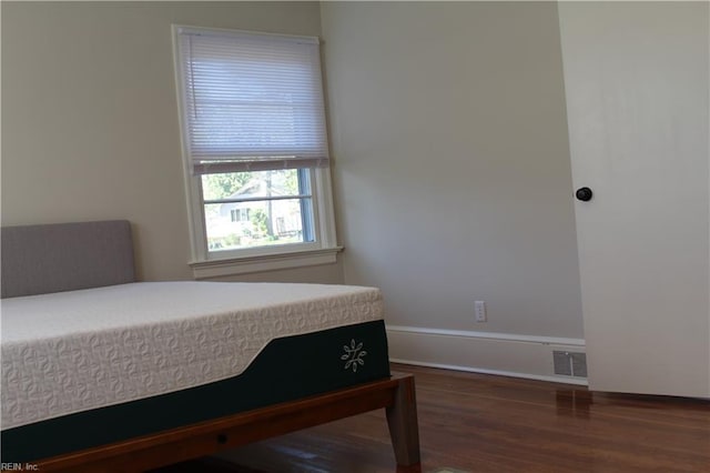 bedroom with baseboards, visible vents, and wood finished floors