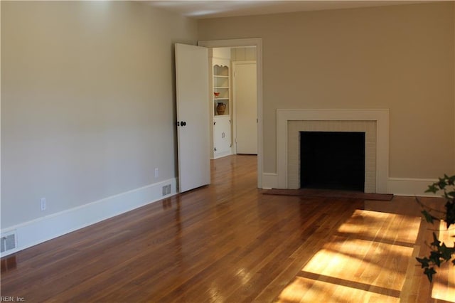 unfurnished living room featuring a brick fireplace, visible vents, baseboards, and wood finished floors