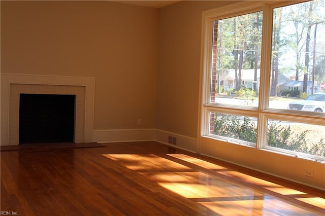 unfurnished living room featuring baseboards, visible vents, wood finished floors, and a fireplace