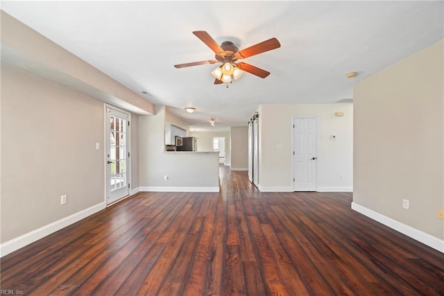 unfurnished living room featuring baseboards, dark wood-type flooring, and a ceiling fan