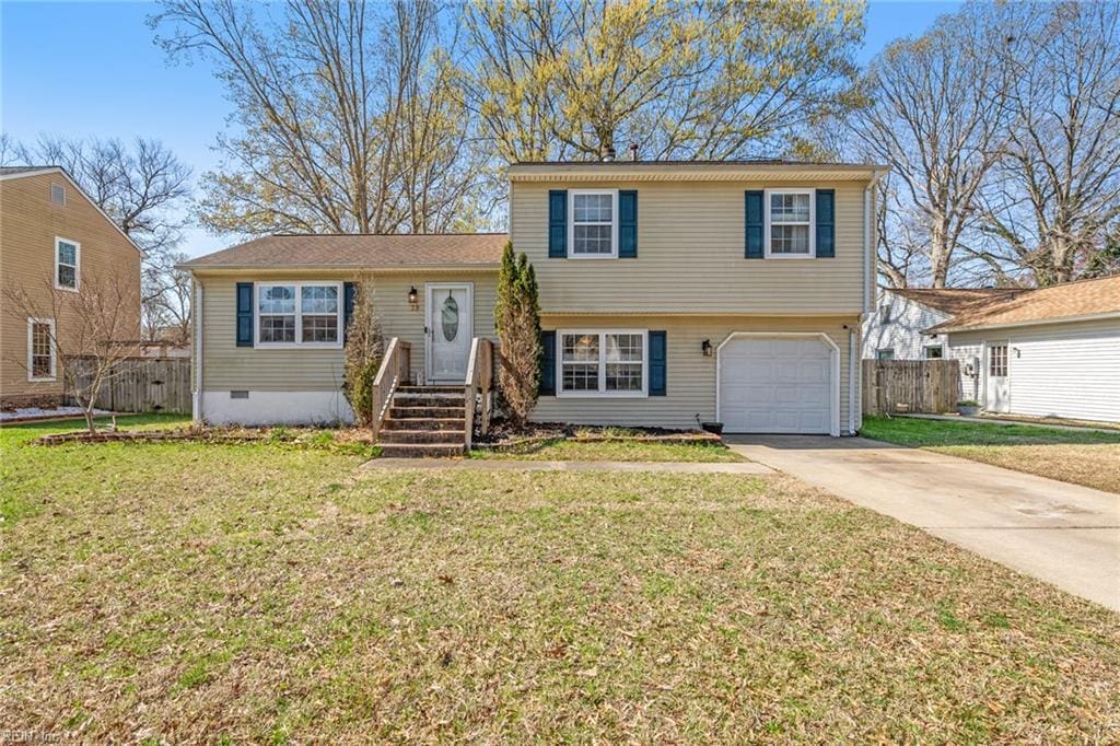 split level home with fence, driveway, a front yard, and a garage