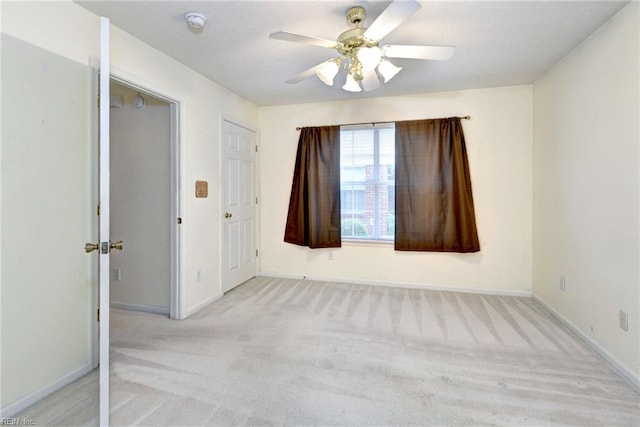 carpeted empty room with a textured ceiling, baseboards, and a ceiling fan