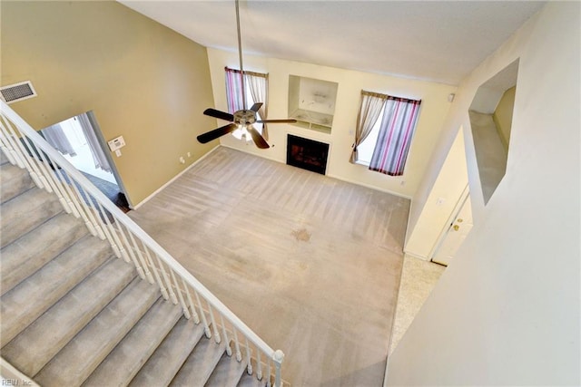 stairway with baseboards, a fireplace, carpet flooring, visible vents, and ceiling fan