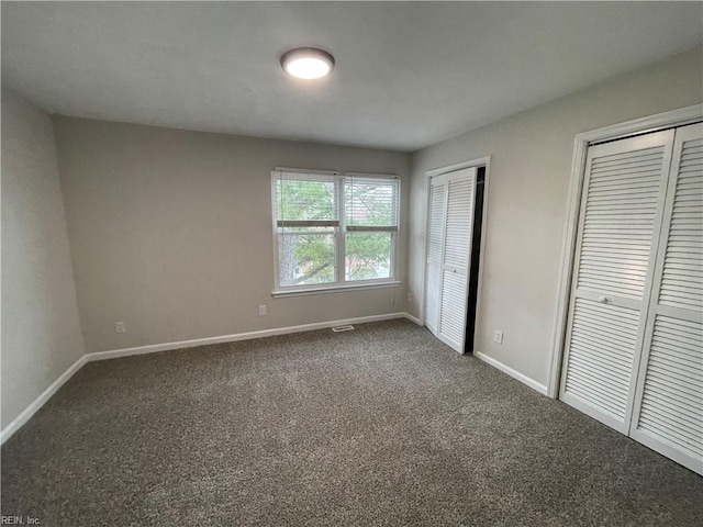 unfurnished bedroom with two closets, baseboards, dark colored carpet, and visible vents
