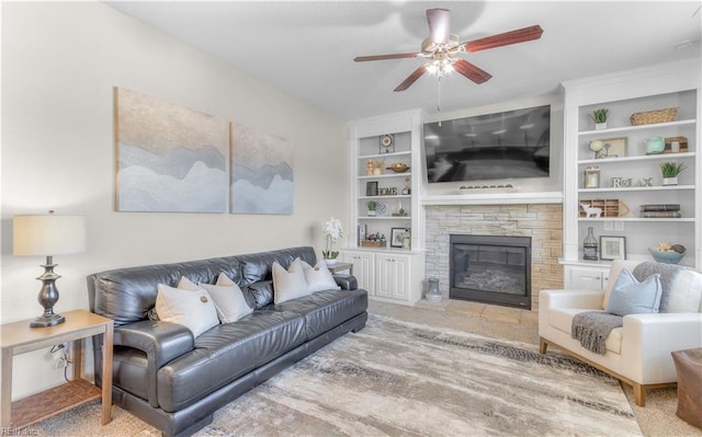 carpeted living area with a fireplace, built in shelves, and ceiling fan