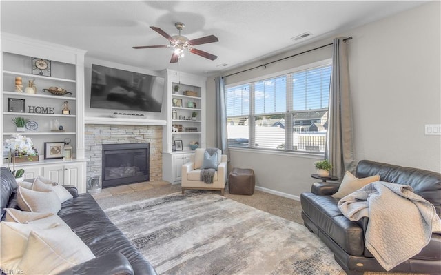 living room with a stone fireplace, built in features, baseboards, ceiling fan, and carpet