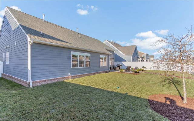 rear view of property featuring a shingled roof, fence, and a lawn