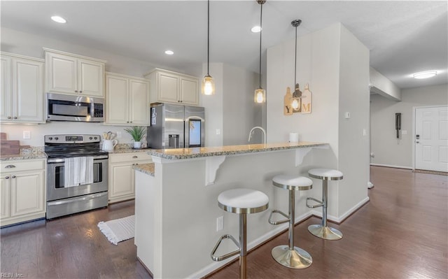 kitchen featuring a breakfast bar area, light stone countertops, a peninsula, stainless steel appliances, and dark wood-type flooring