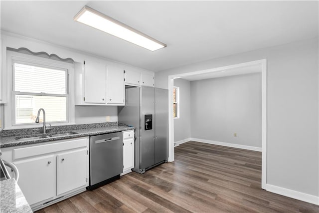 kitchen with a sink, appliances with stainless steel finishes, dark wood-style floors, baseboards, and white cabinets