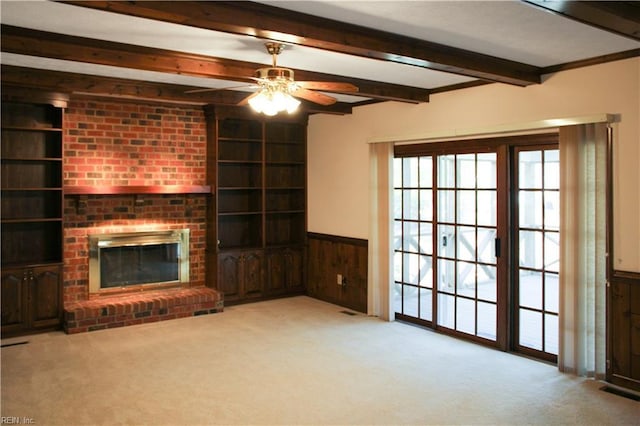 unfurnished living room featuring a wainscoted wall, carpet floors, beam ceiling, and built in shelves