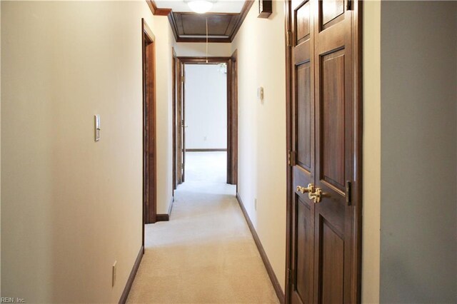 corridor featuring baseboards, ornamental molding, attic access, and light carpet