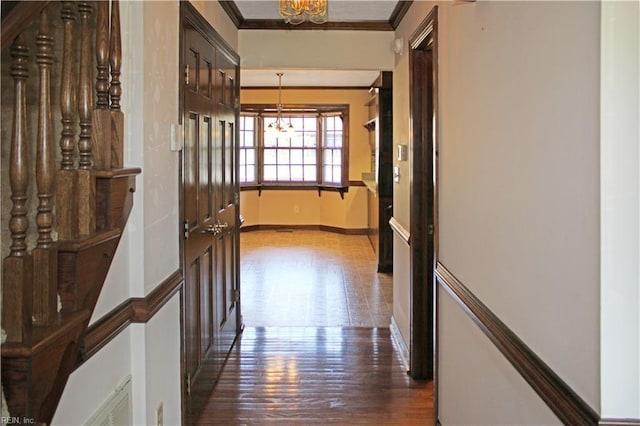 corridor featuring dark wood-style floors, crown molding, baseboards, and a chandelier